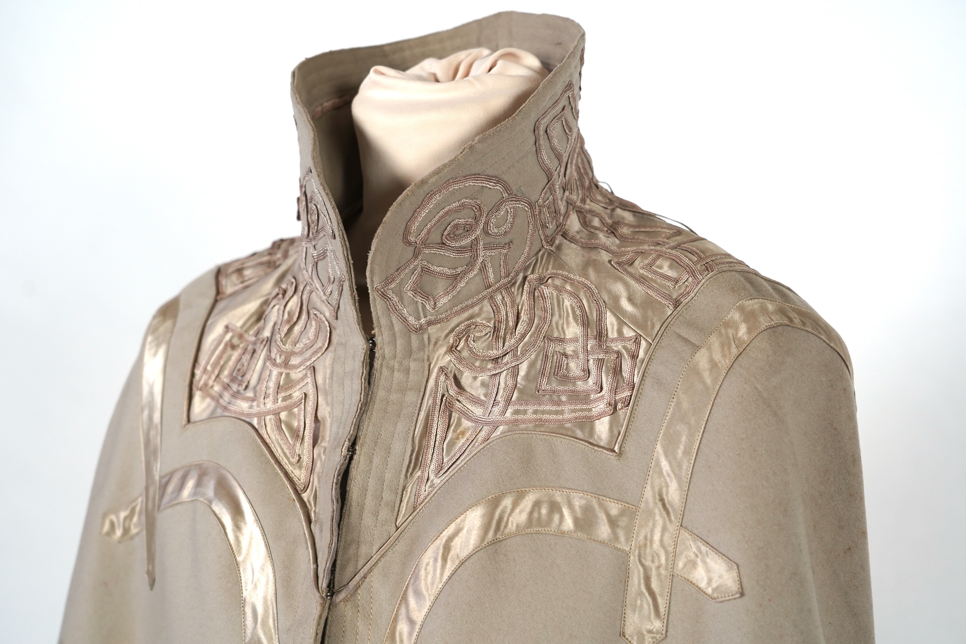 An Edwardian mushroom wool evening cape, decorated with silk ribbon worked strapping and ornate appliquéd fine braiding across the shoulders and under section of the collar, lined with cream silk satin.